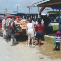 People gather around a truck filled with cardboard boxes at an outdoor distribution event.