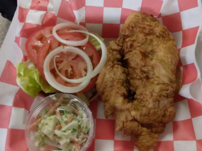A breaded chicken sandwich with lettuce, tomato, and onion, served with a side of coleslaw in a red-and-white checkered tray.