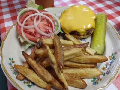 A cheeseburger with tomato, onion, and lettuce, served with a side of french fries and a pickle on a floral plate.