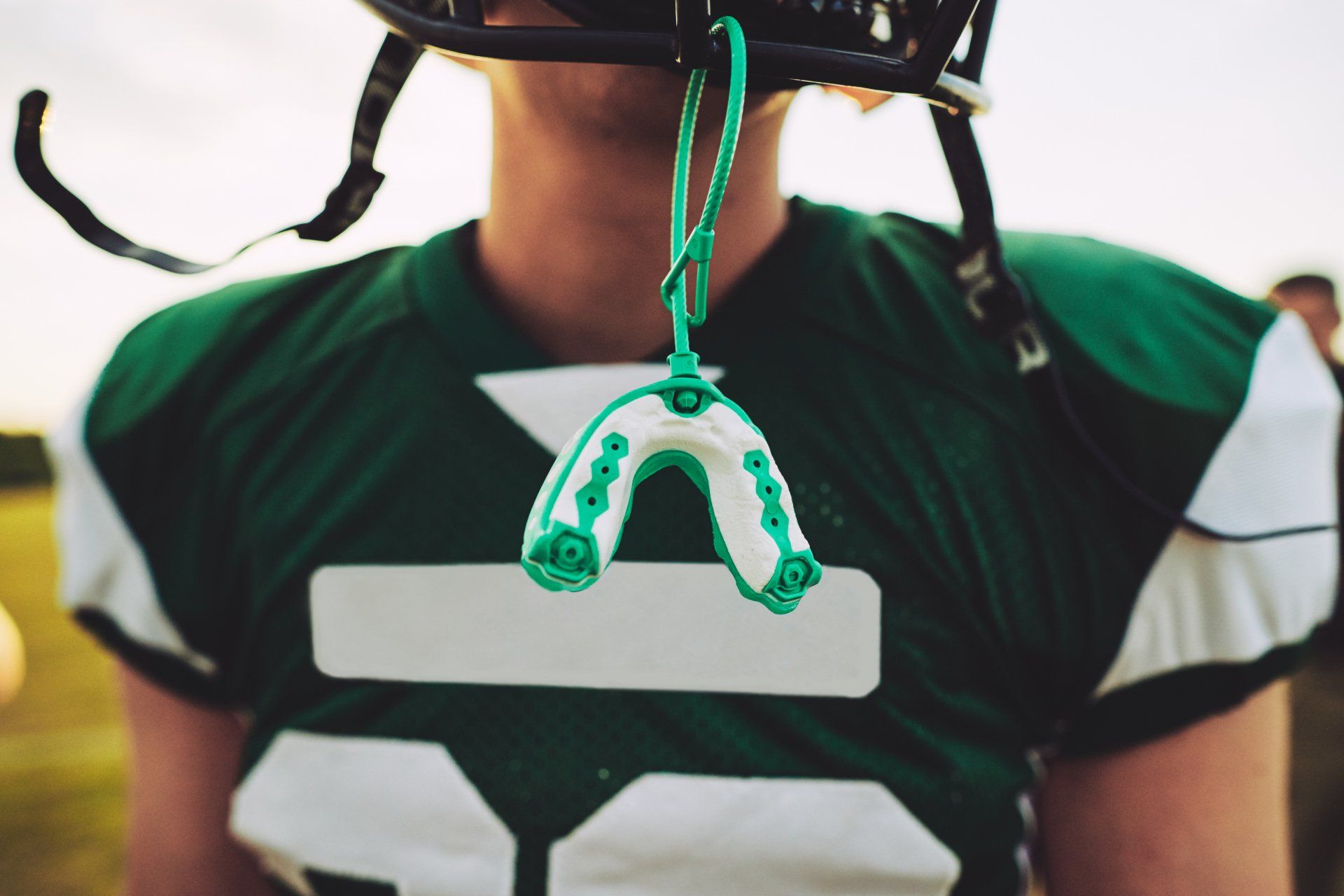 person standing outside in a football jersey and helmet focusing in on a mouthguard hanging from helmet