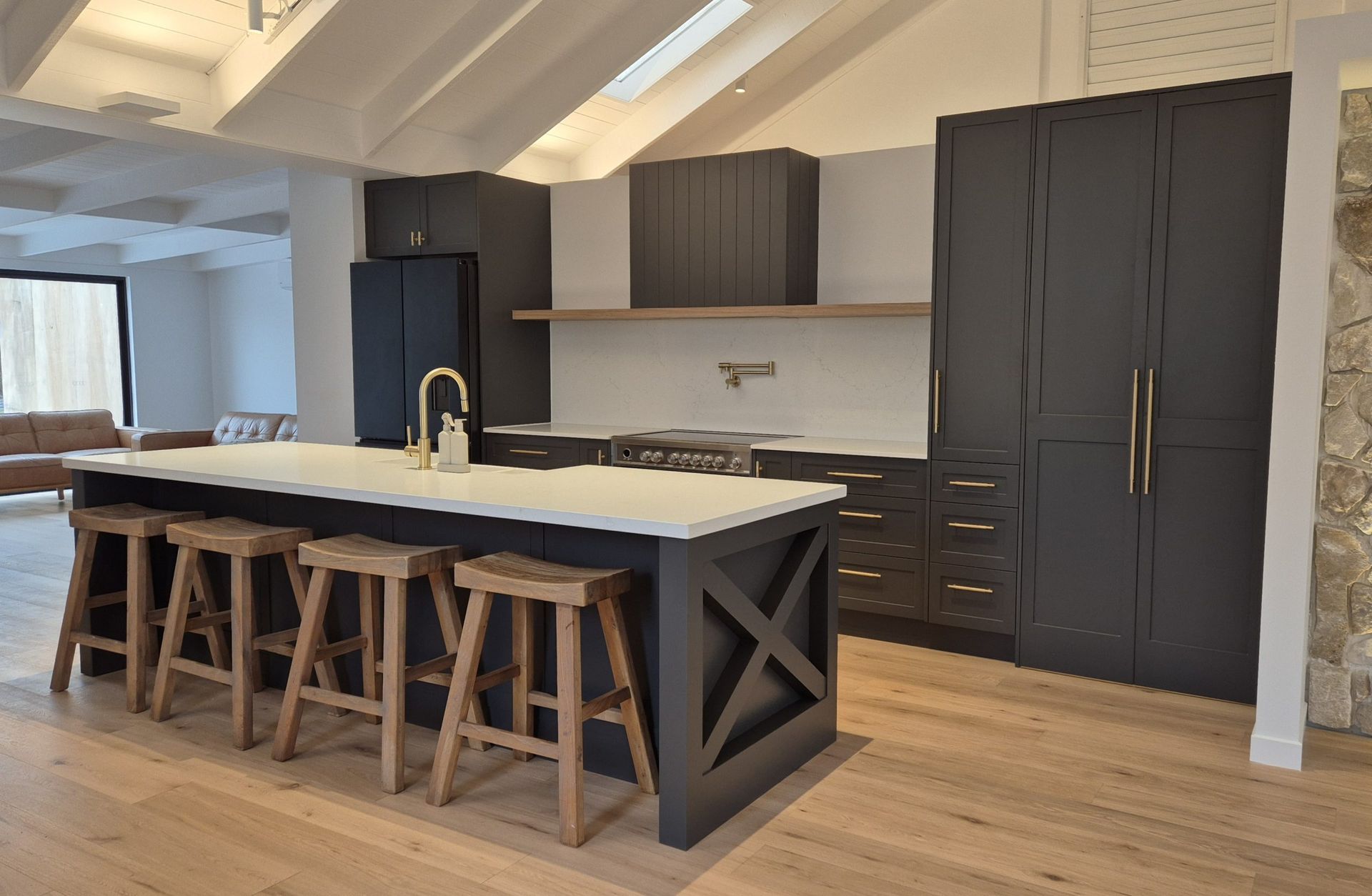 Modern kitchen with a large island, bar stools, dark cabinets, and wood floors in a bright room