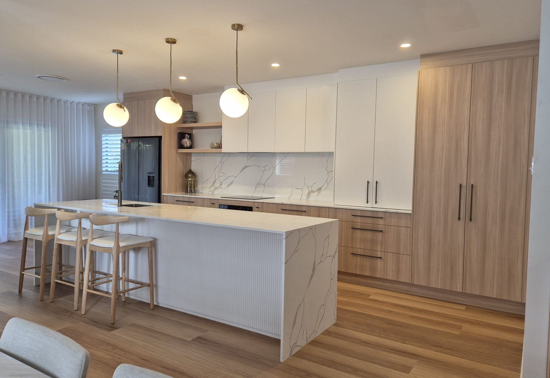 Bright modern kitchen with white island, wood floors, pendant lights, and bar stools