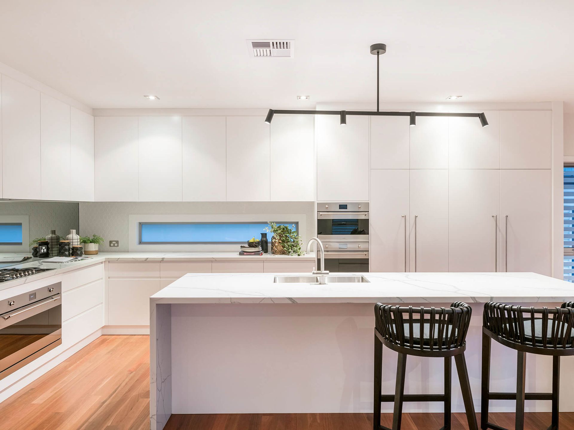 Modern white kitchen with island, black bar stools, and wood flooring