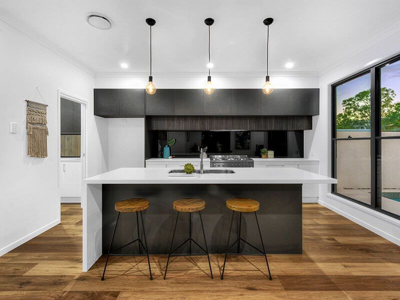 Modern kitchen with white island, dark cabinets, three bar stools, and large windows overlooking greenery