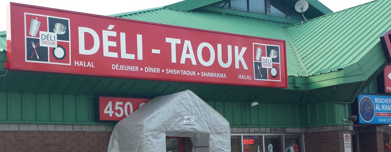 Vue extérieure du restaurant Déli-Taouk avec son enseigne rouge. L'auvent est une structure grise en forme de tente. Le numéro 450 est visible.