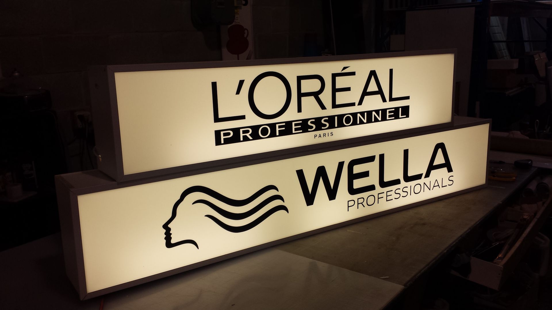 Two backlit signs: L'Oréal Professionnel and Wella Professionals logos in a salon setting.