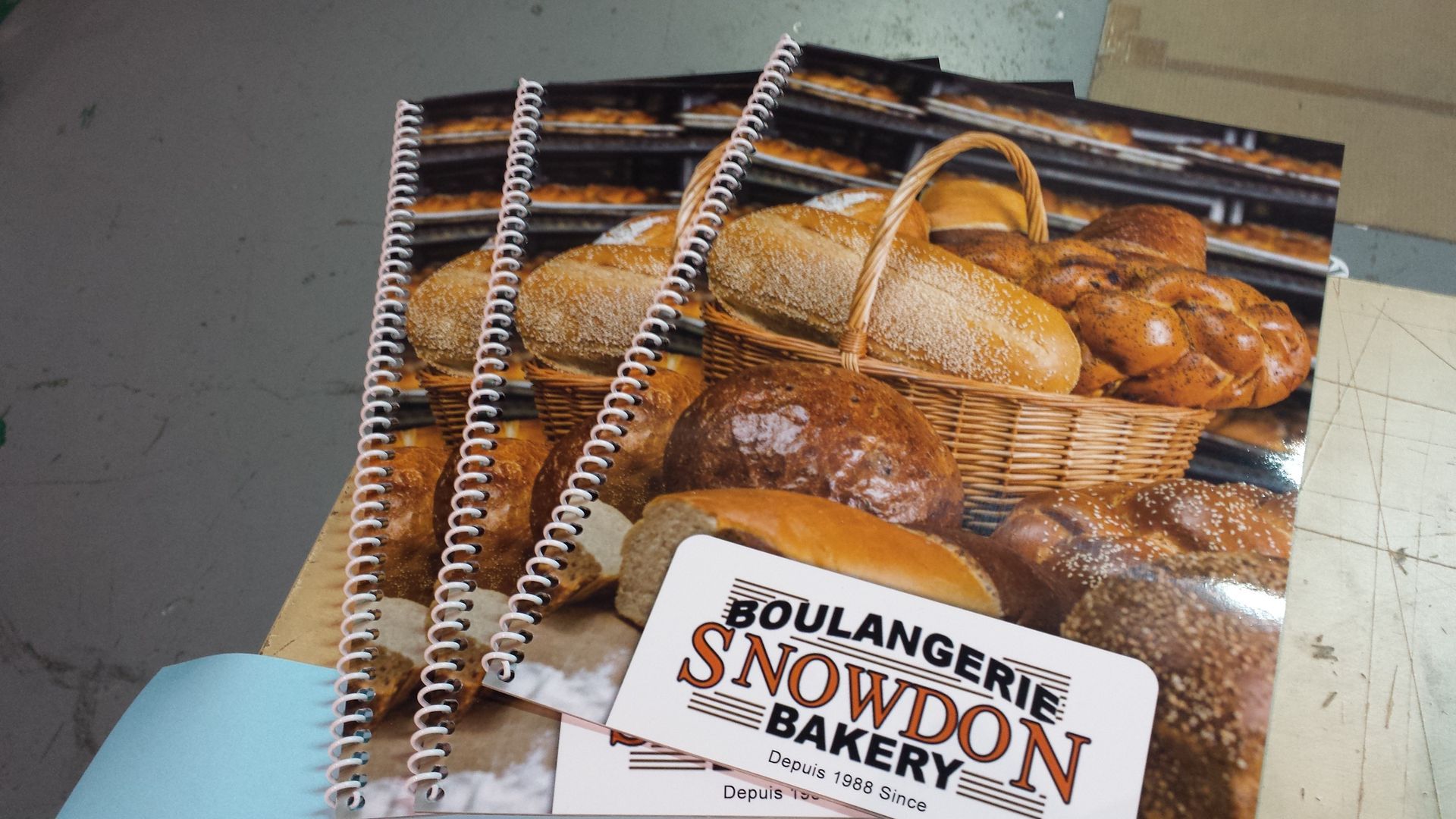 Stack of bound bakery brochures with bread basket on the cover, branded