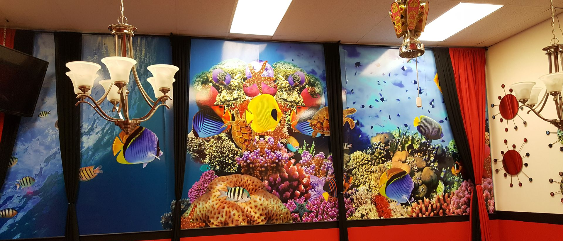 Room with aquarium wall mural, chandeliers, and red accents.