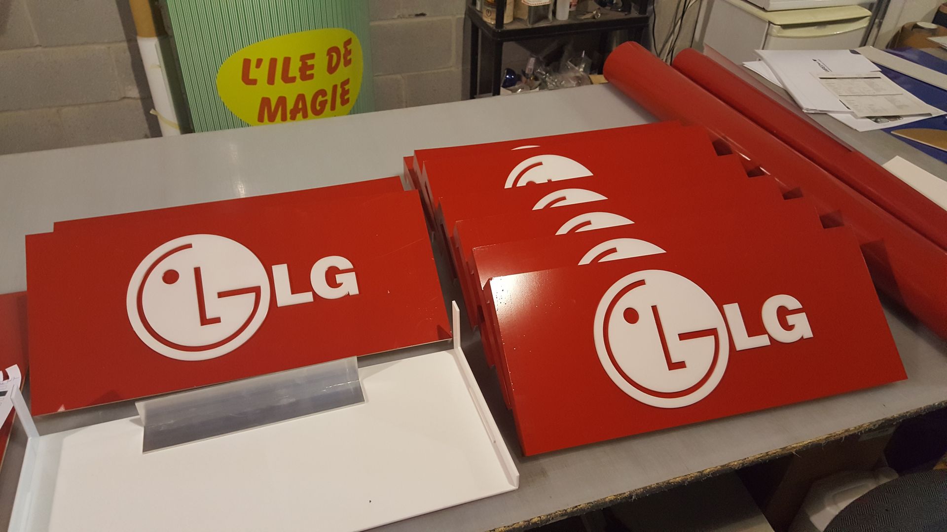 Panneaux LG rouges avec logos blancs sur une table. Une boîte découpée se trouve sous le panneau plus petit, avec d'autres éléments en arrière-plan.