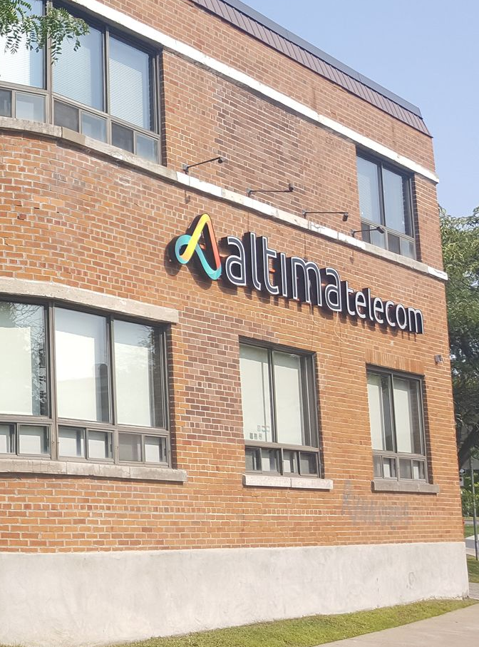 Bâtiment en briques avec un panneau indiquant « Aaltima telecom » avec le logo en jaune et vert.