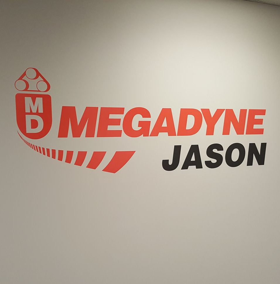 Megadyne Jason logo on a wall; red and black text with a graphic of a belt on white background.