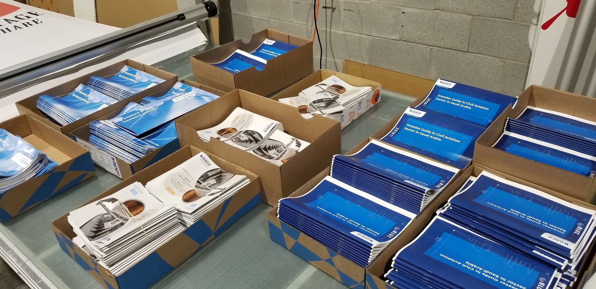 Boxes of blue and white brochures on a table in a warehouse or print shop.