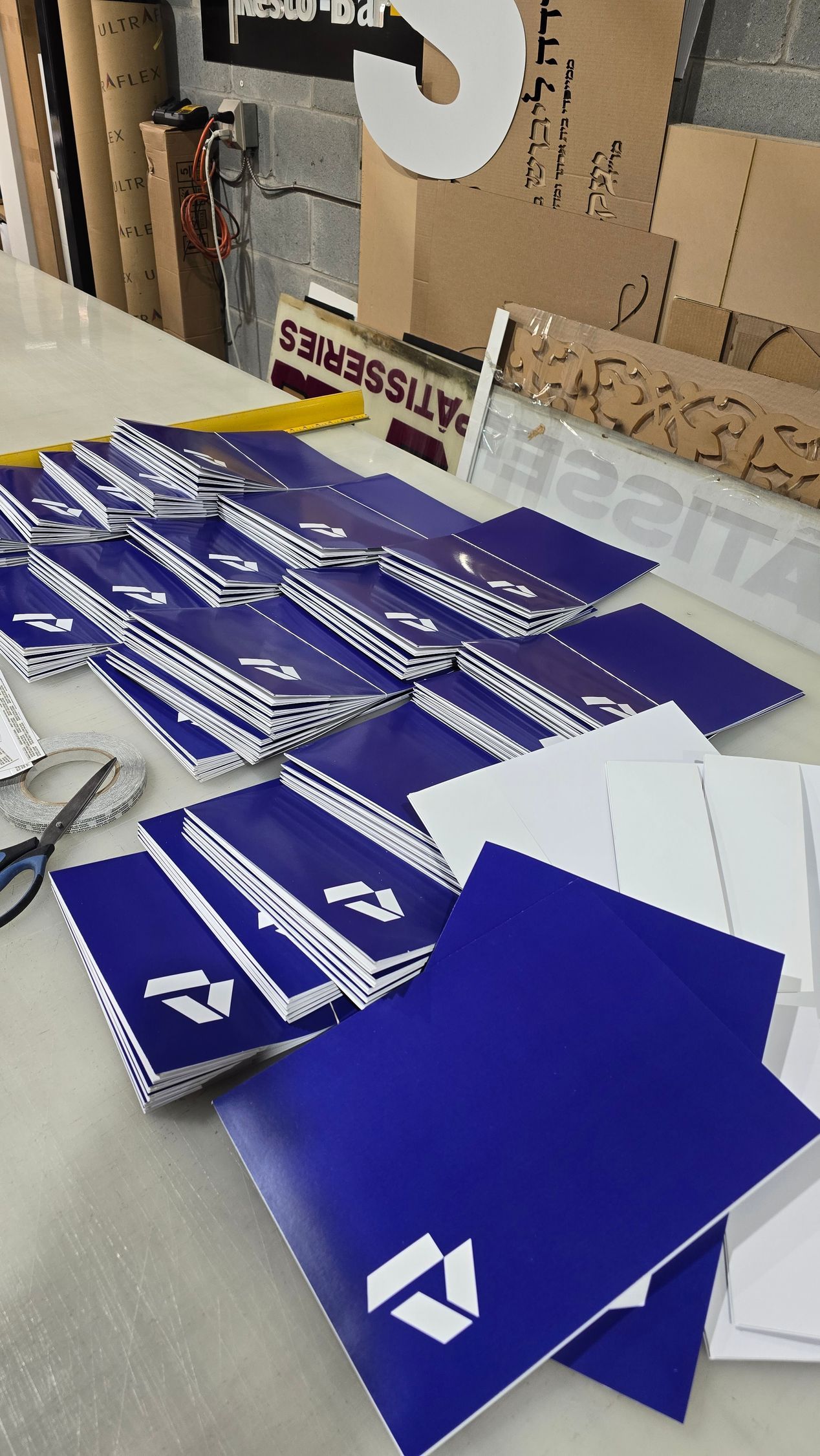 Blue and white branded notebooks stacked on a table. Scissors and materials are nearby.