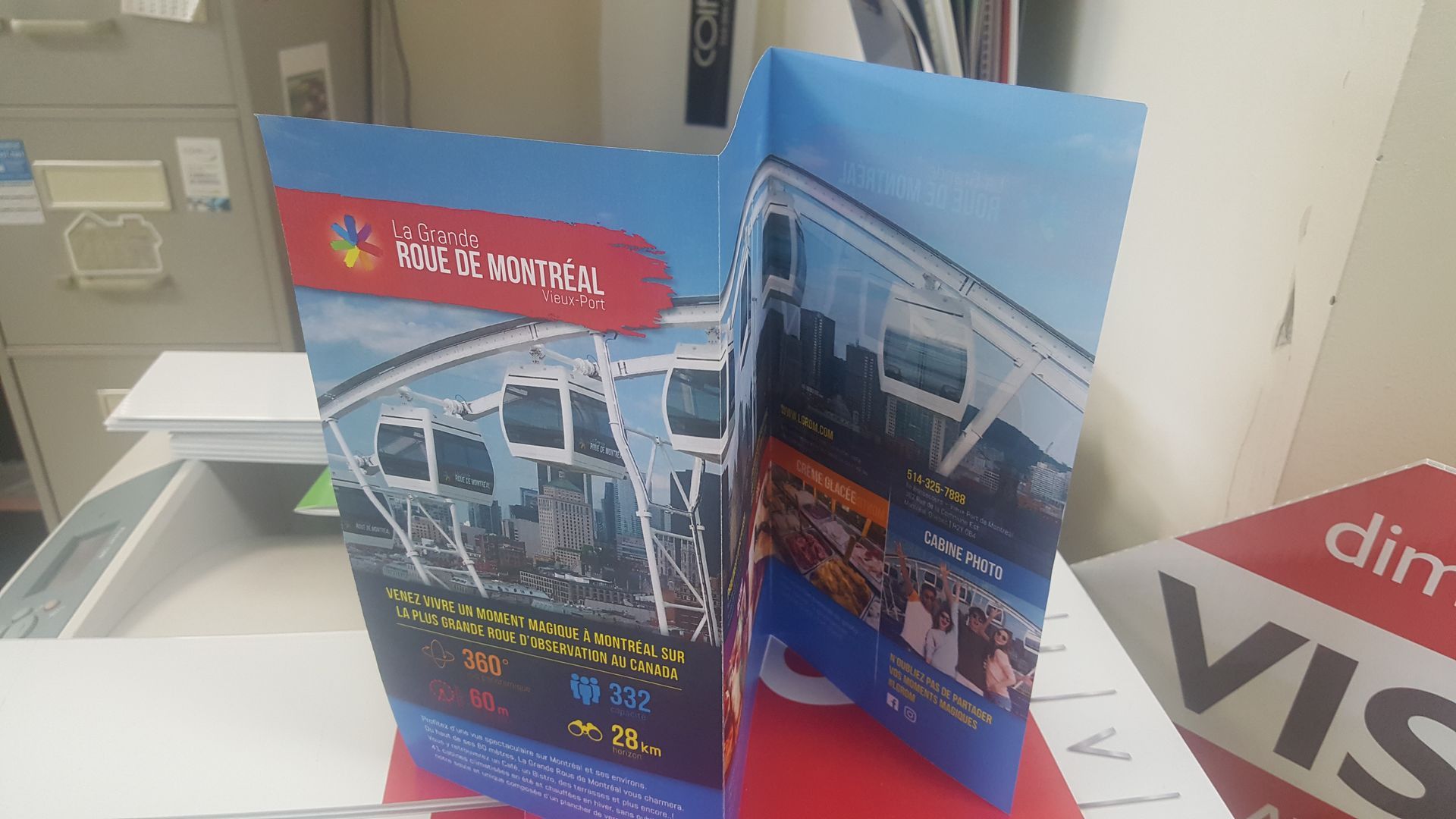 Brochure publicitaire pour une attraction de grande roue, avec des téléphériques et un ciel bleu.
