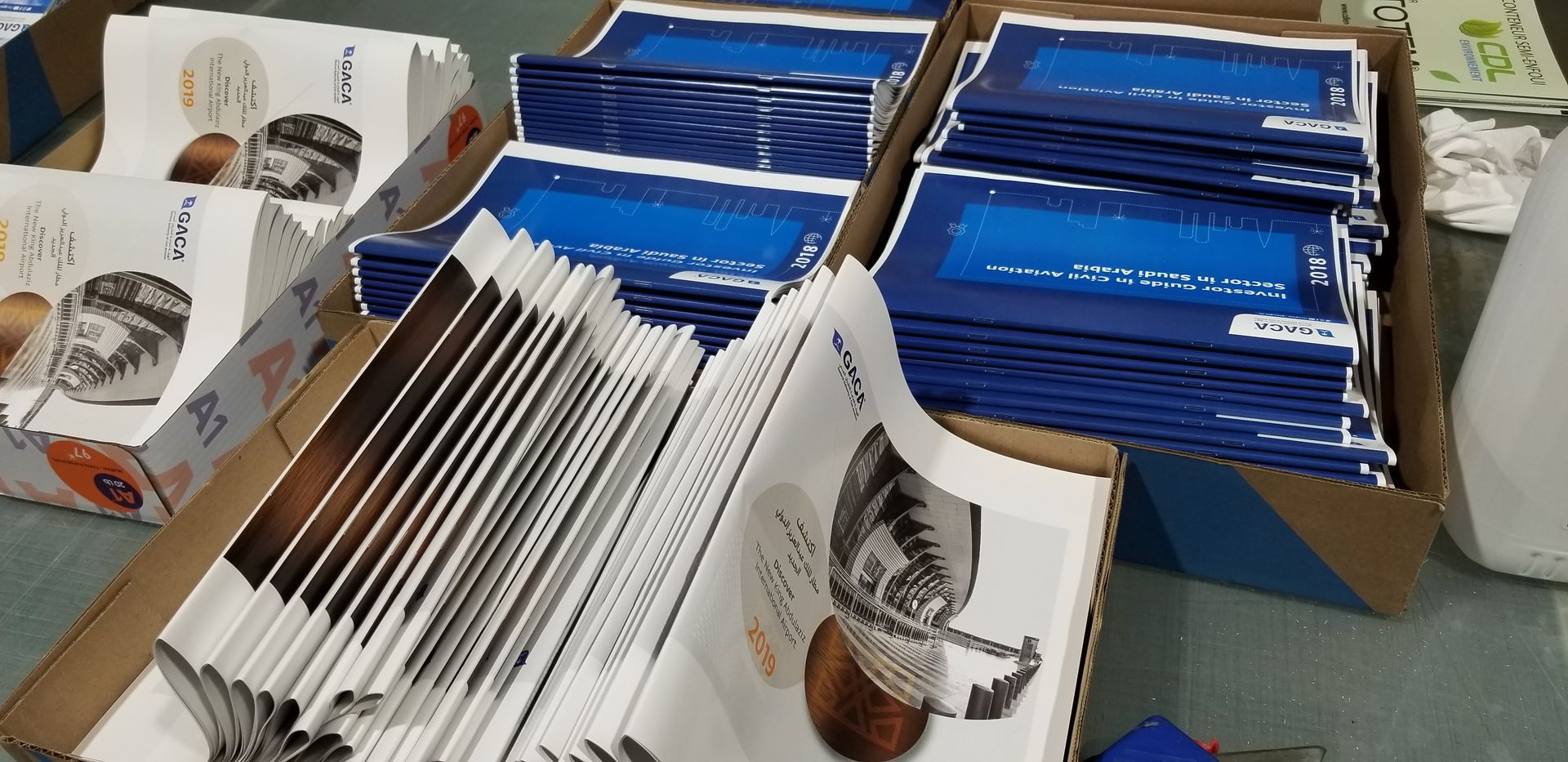 Piles d'enveloppes bleues et de brochures de produits dans des boîtes en carton, probablement destinées à l'envoi postal.
