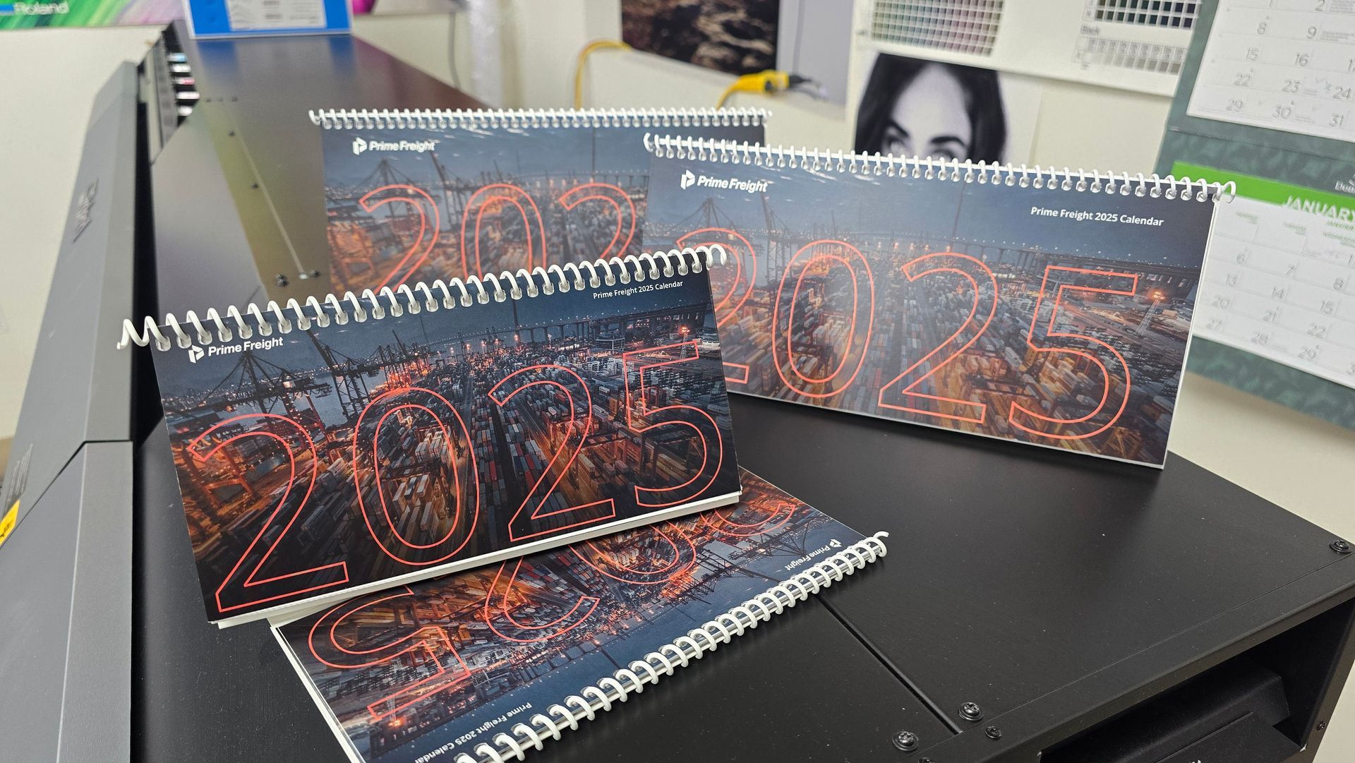 Several 2023 calendars with a landscape image and spiral binding are stacked on a black machine.