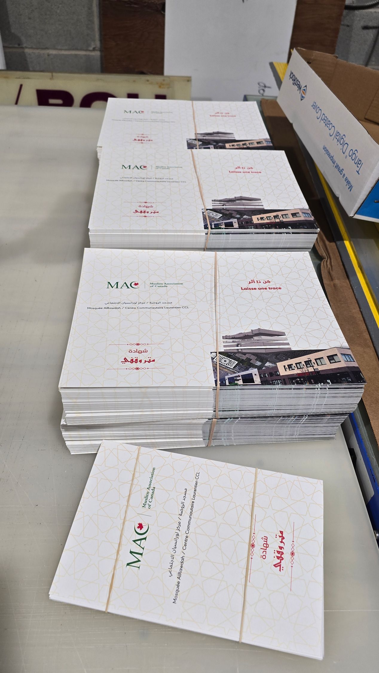 Des piles de brochures blanches attachées avec des élastiques, présentant des bâtiments et du texte sur une table.