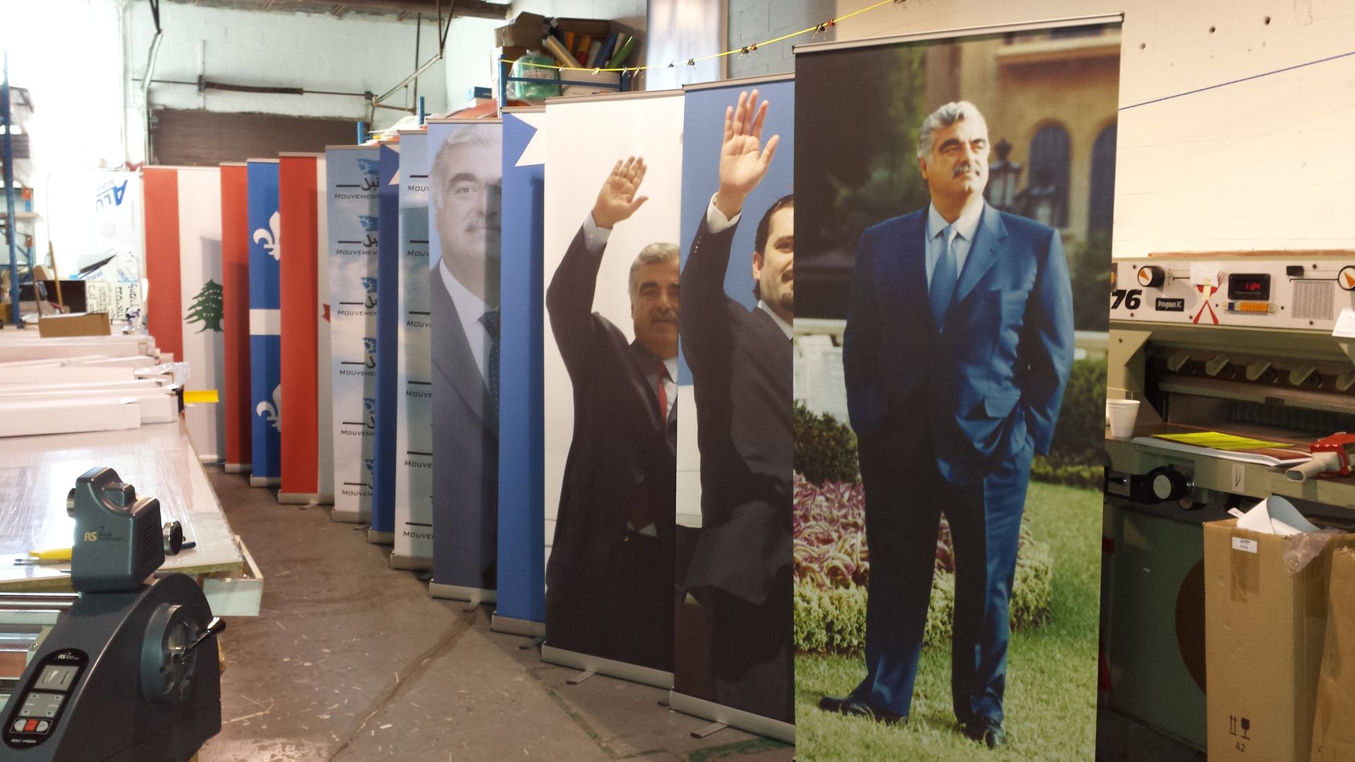 Une rangée de grandes affiches représentant un homme en costume saluant, alignées à l'intérieur d'un atelier.