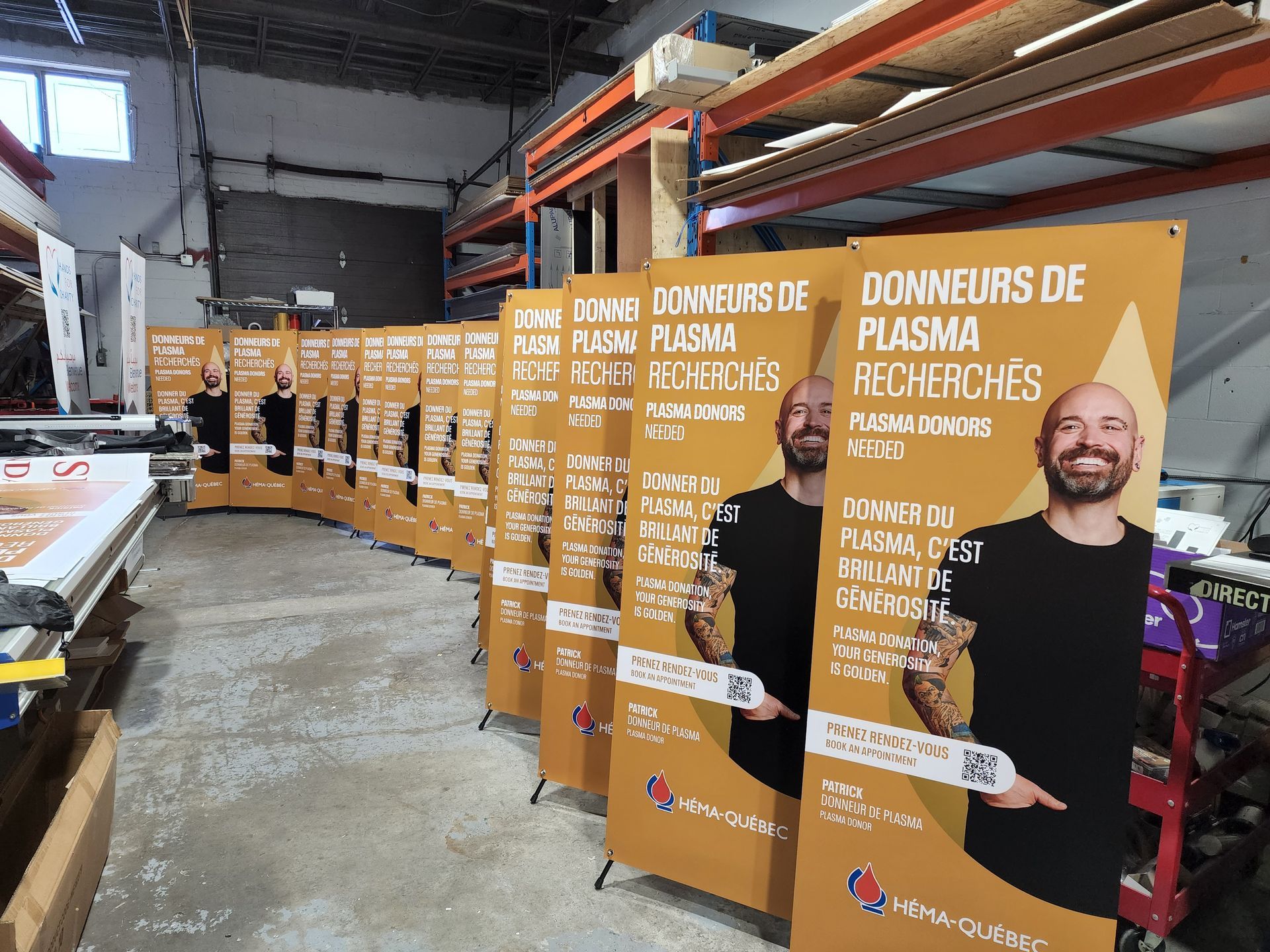 Rangée de banderoles pour le don de plasma dans un entrepôt. Chacune arbore la photo d'un homme, un fond doré et un texte en français.