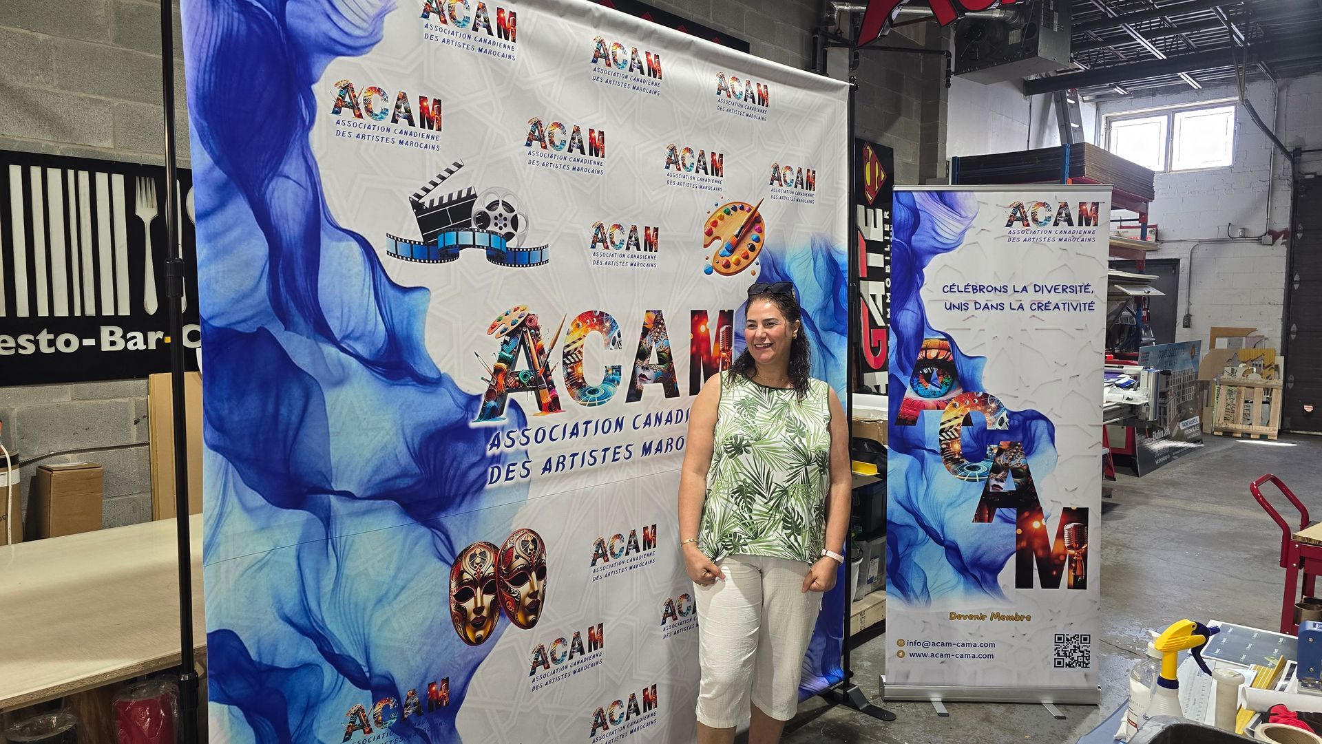 Une femme se tient entre deux banderoles portant le logo « ACAU ». Intérieur.