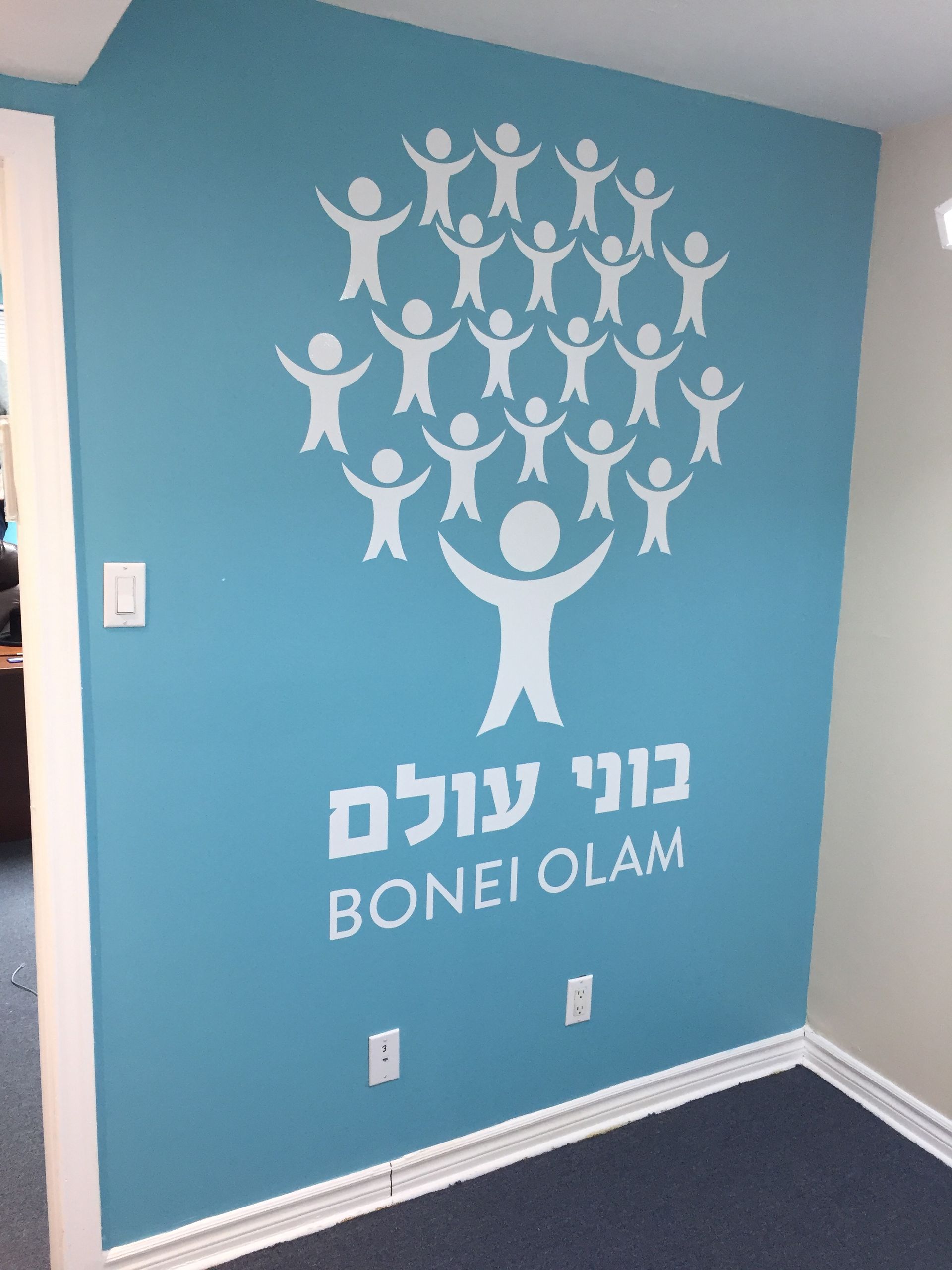 White graphic of people-tree on a blue wall with Hebrew/English text 