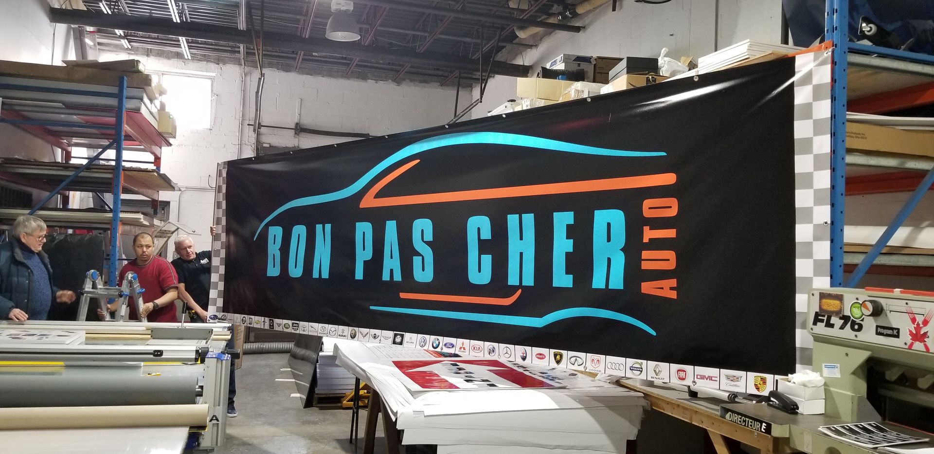 Des gens affichant une bannière avec le logo Bon Pas Cher Auto dans un entrepôt.