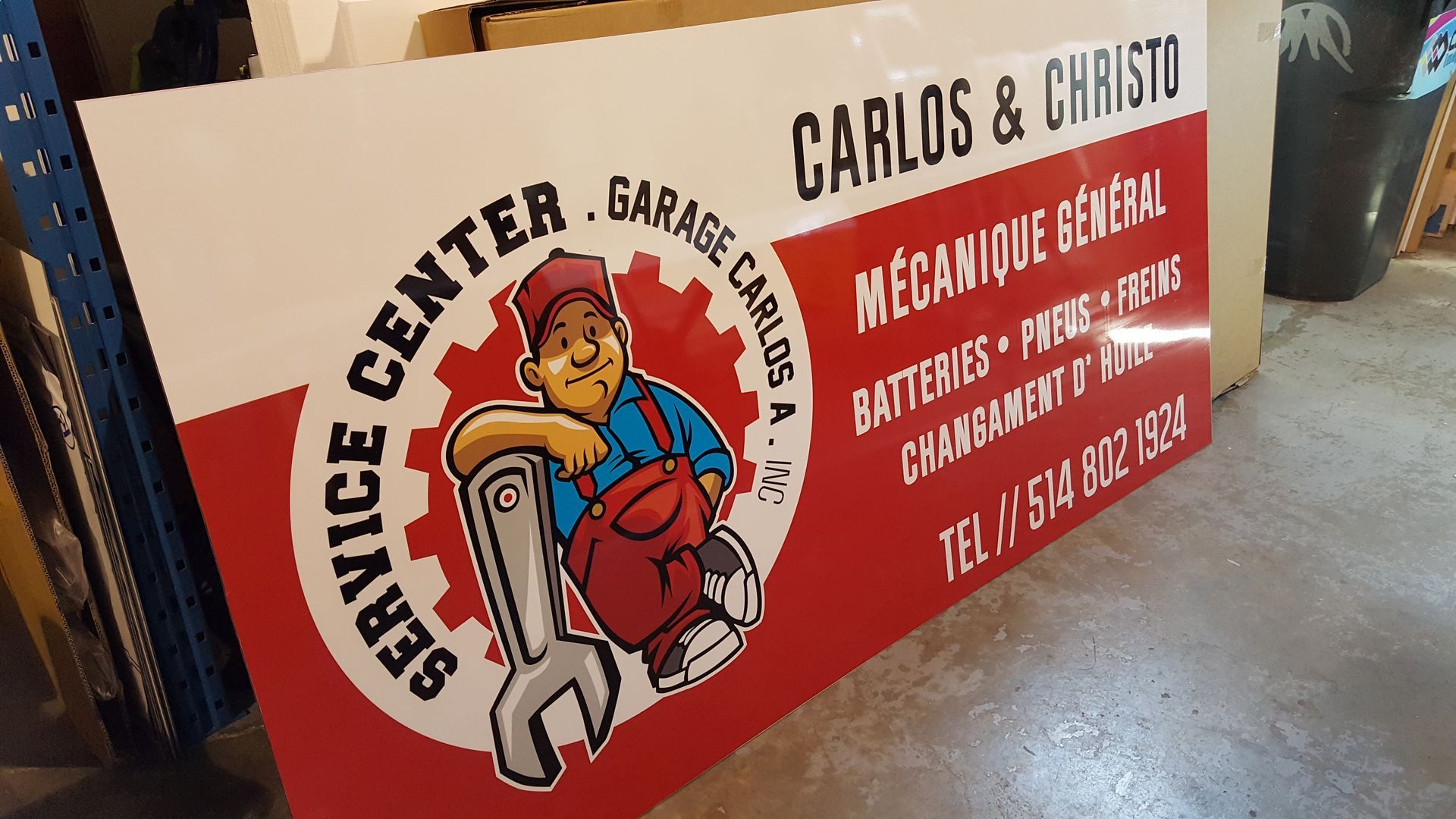 Panneau pour le garage Carlos & Christ : rouge, blanc et noir, représentant un mécanicien.