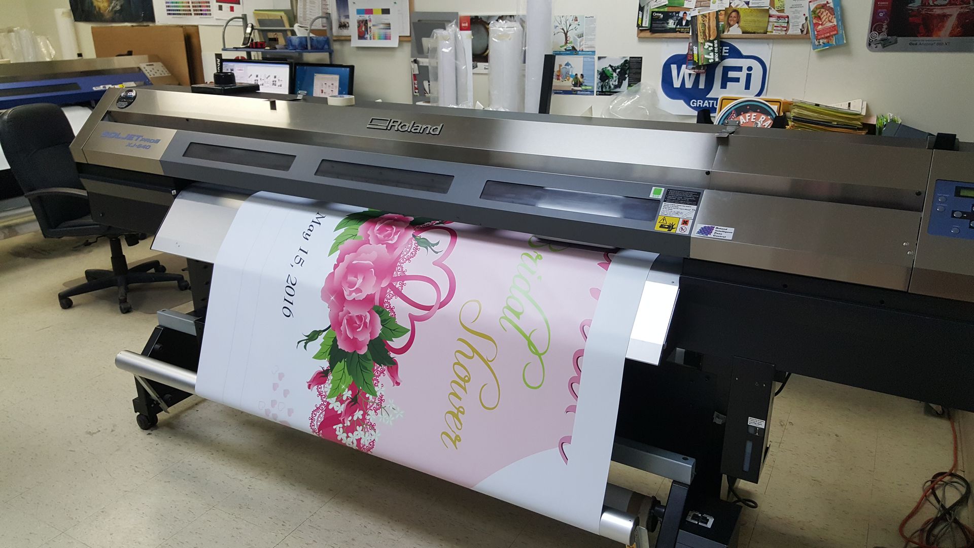 Imprimante grand format imprimant une bannière « douche nuptiale » avec un motif floral rose.