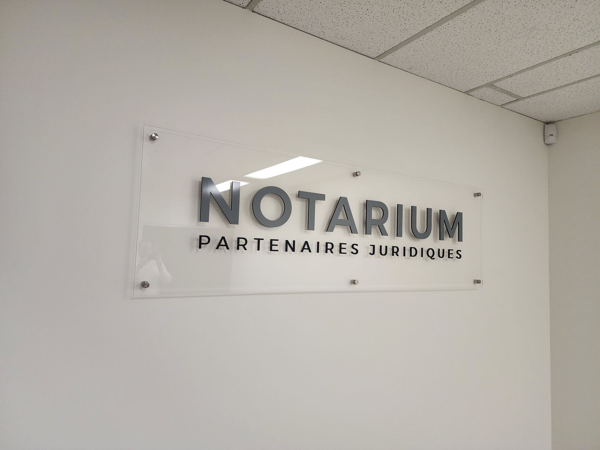 Panneau sur mur blanc : « NOTARIUM » au-dessus de « PARTENAIRES JURIDIQUES », monté avec des entretoises argentées.