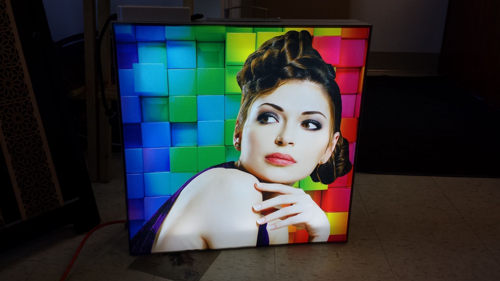 Portrait d'une femme sur un boîtier LED coloré. L'arrière-plan présente un motif cubique.