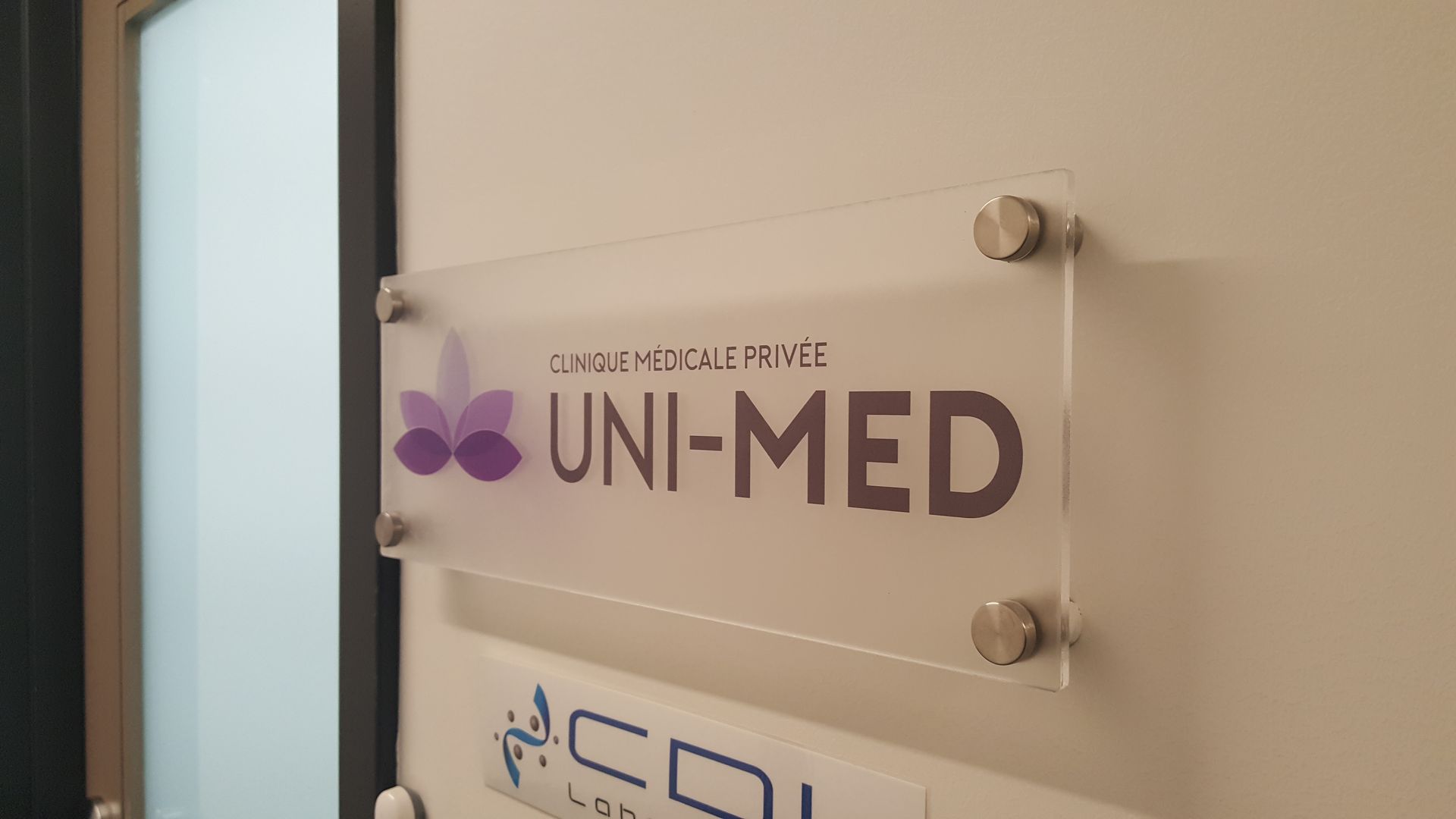 Panneau pour la clinique UNI-MED sur un mur, avec logo et texte en violet et gris foncé.