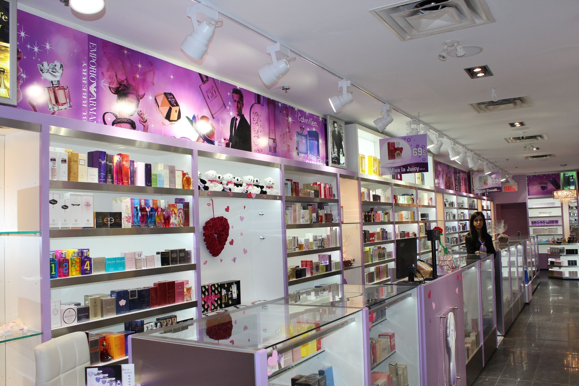Intérieur d'une parfumerie avec des étagères de présentation de bouteilles colorées, une caisse et un membre du personnel.