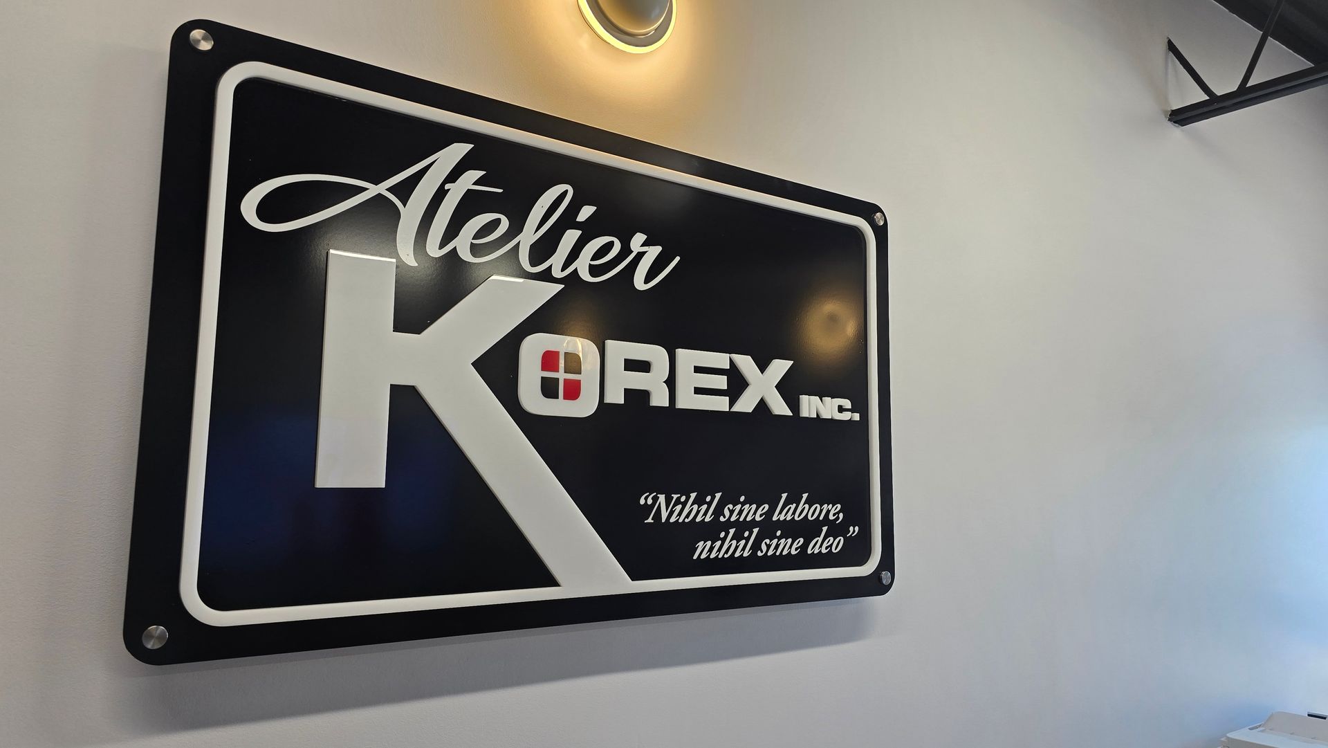 Enseigne pour Atelier Korex Pro sur un mur blanc, design noir et blanc, avec une lumière au dessus.