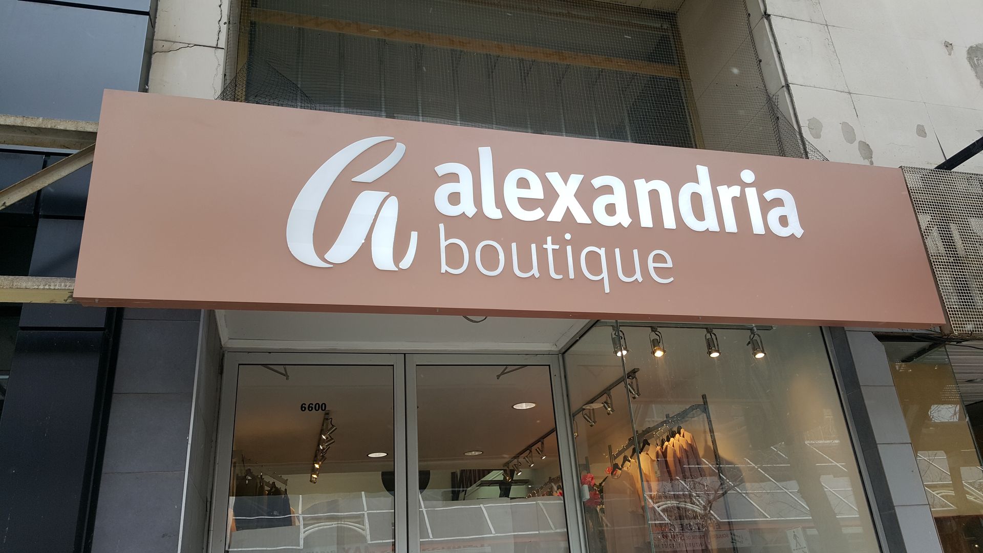 Panneau pour « Boutique Alexandria », avec texte blanc sur fond rectangulaire marron au-dessus de l'entrée d'un magasin.