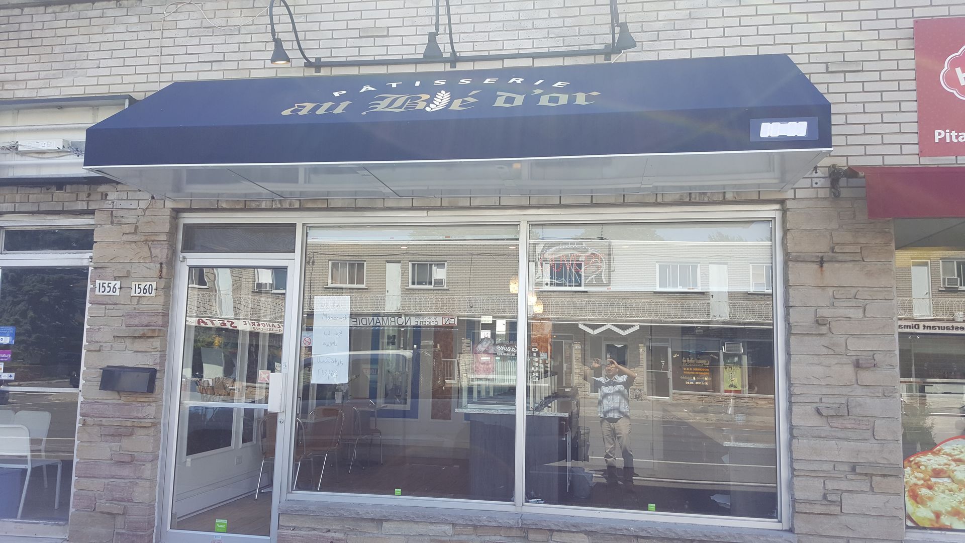 Une devanture avec un auvent bleu foncé, une façade en briques et de grandes fenêtres en verre.