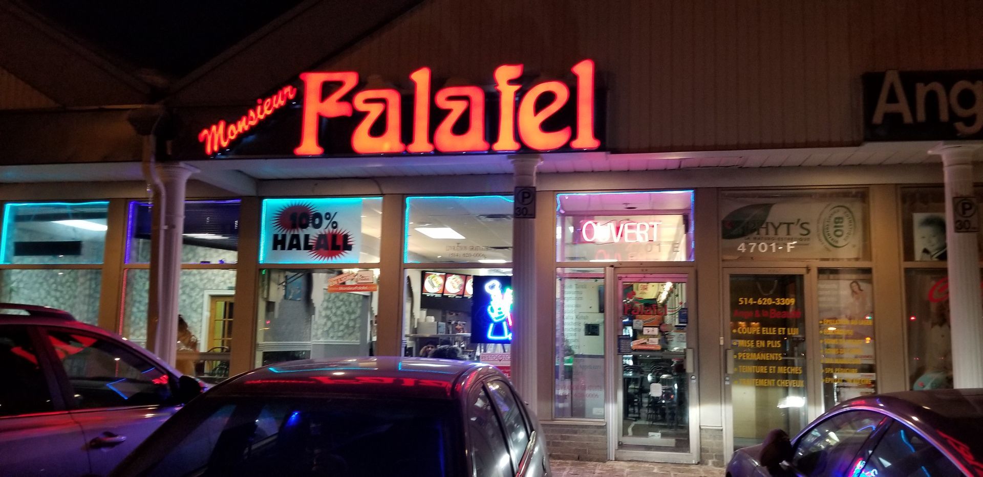 Devanture du restaurant Monsieur Falafel avec enseigne au néon orange vif, voitures devant.