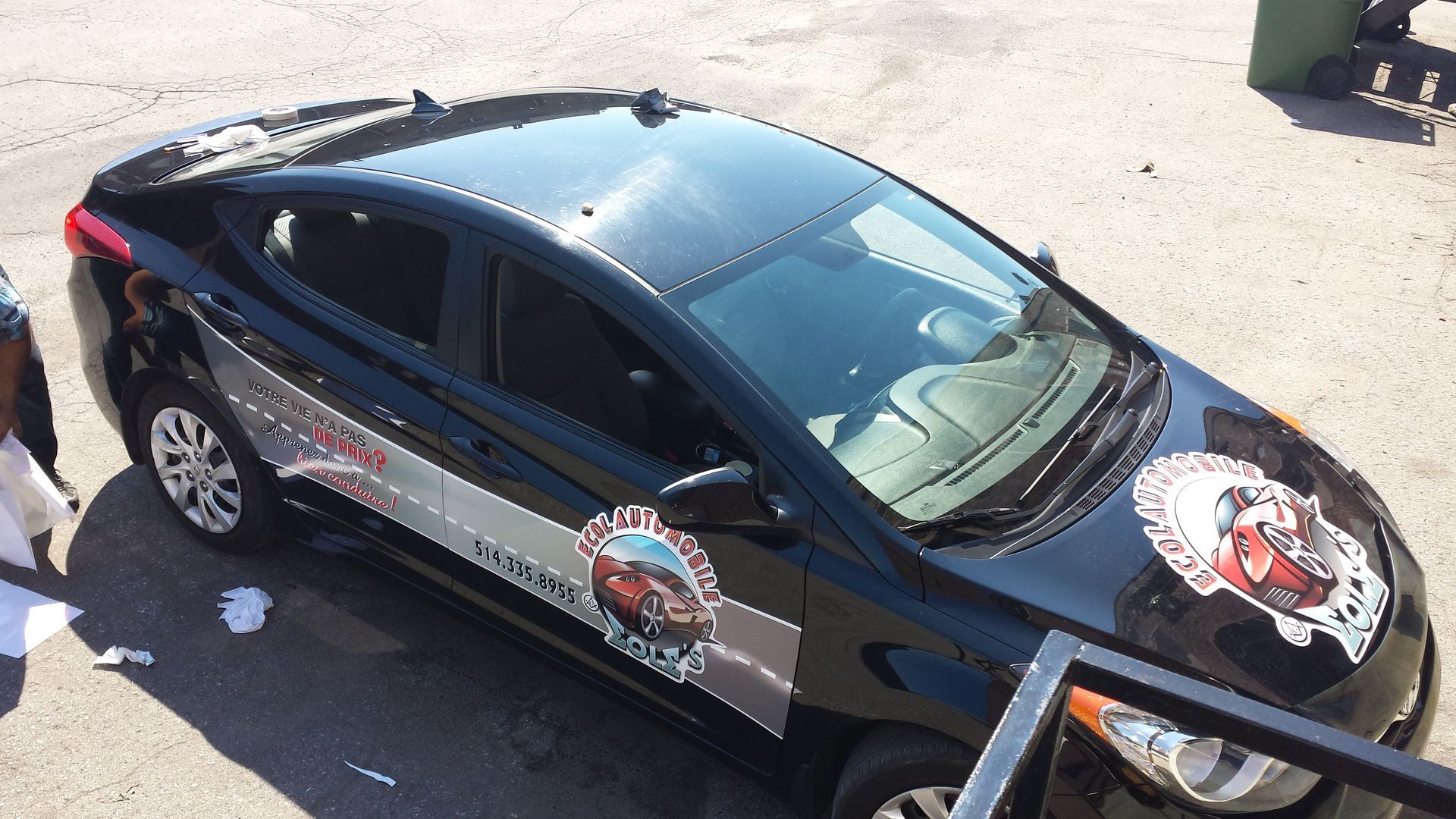 Hyundai Elantra noire avec graphismes publicitaires sur le côté et le capot, garée à l'extérieur sur l'asphalte.