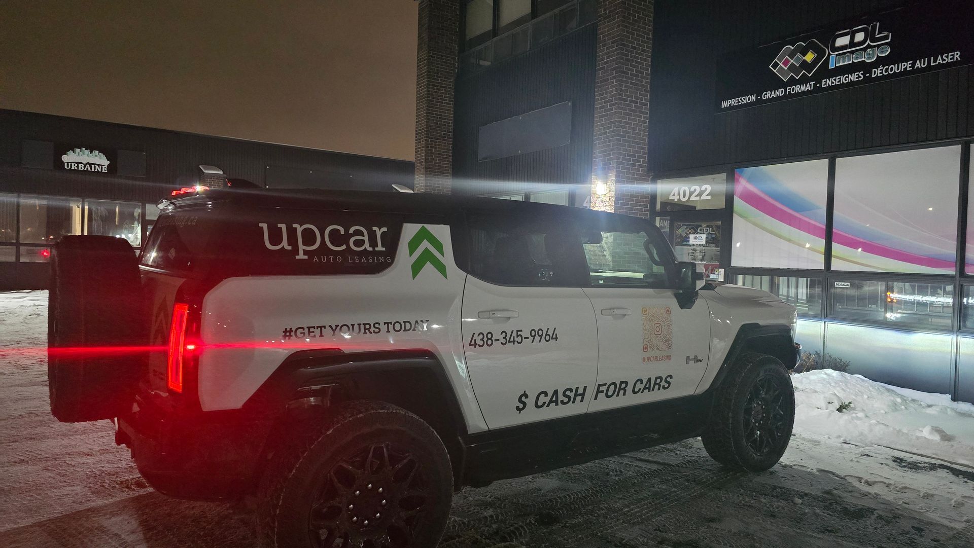 Hummer EV blanc « Upcar » garé près d'un bâtiment la nuit, sol enneigé.