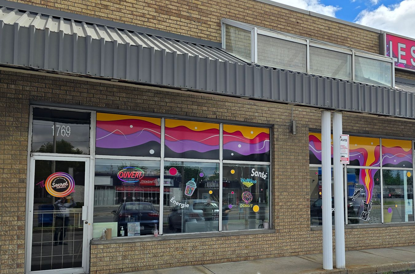 Devanture de magasin avec des fenêtres colorées, un extérieur en brique et un auvent en métal ondulé.