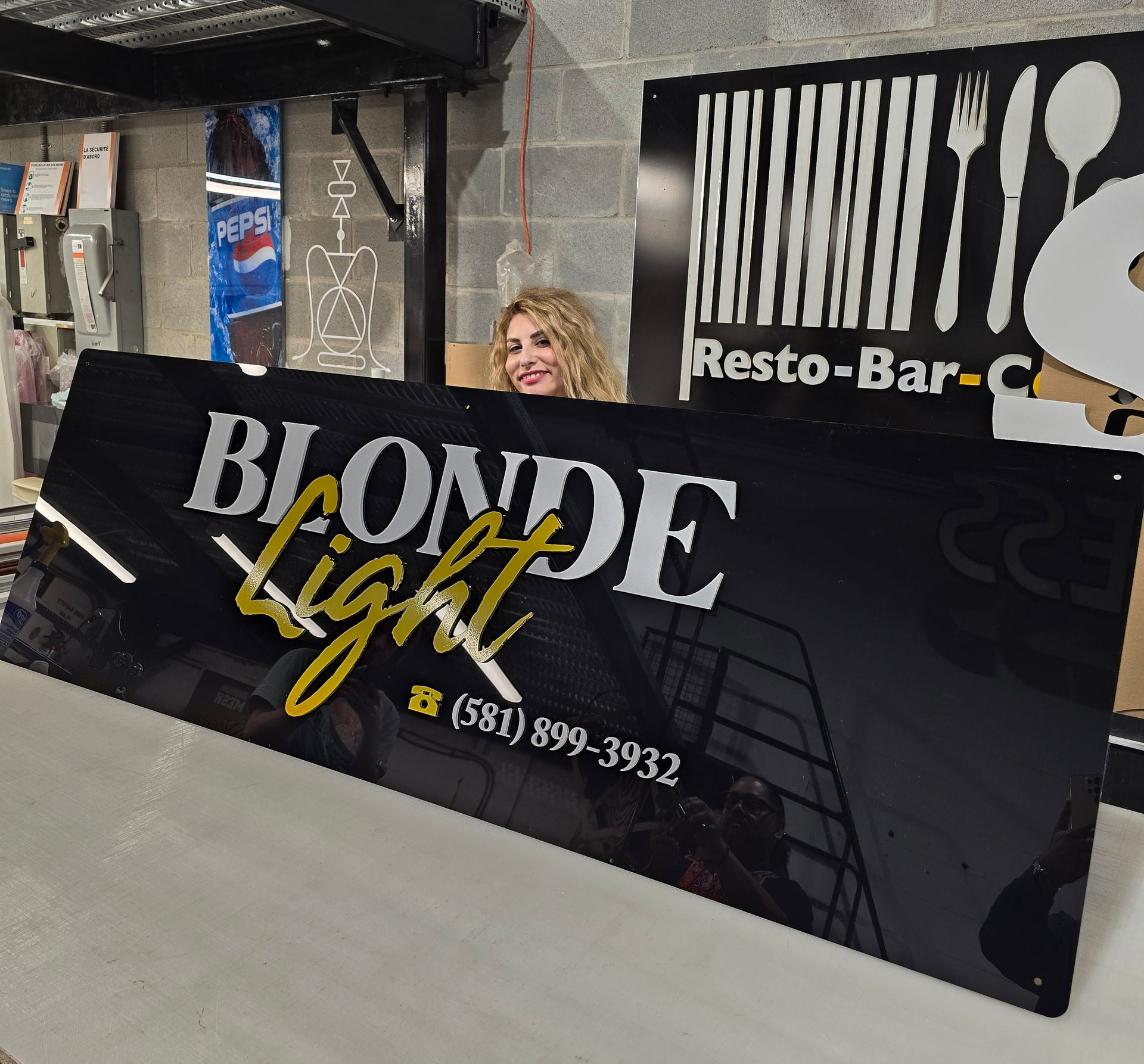 Une femme derrière un panneau noir sur lequel est écrit « Blonde Light » avec un numéro de téléphone.