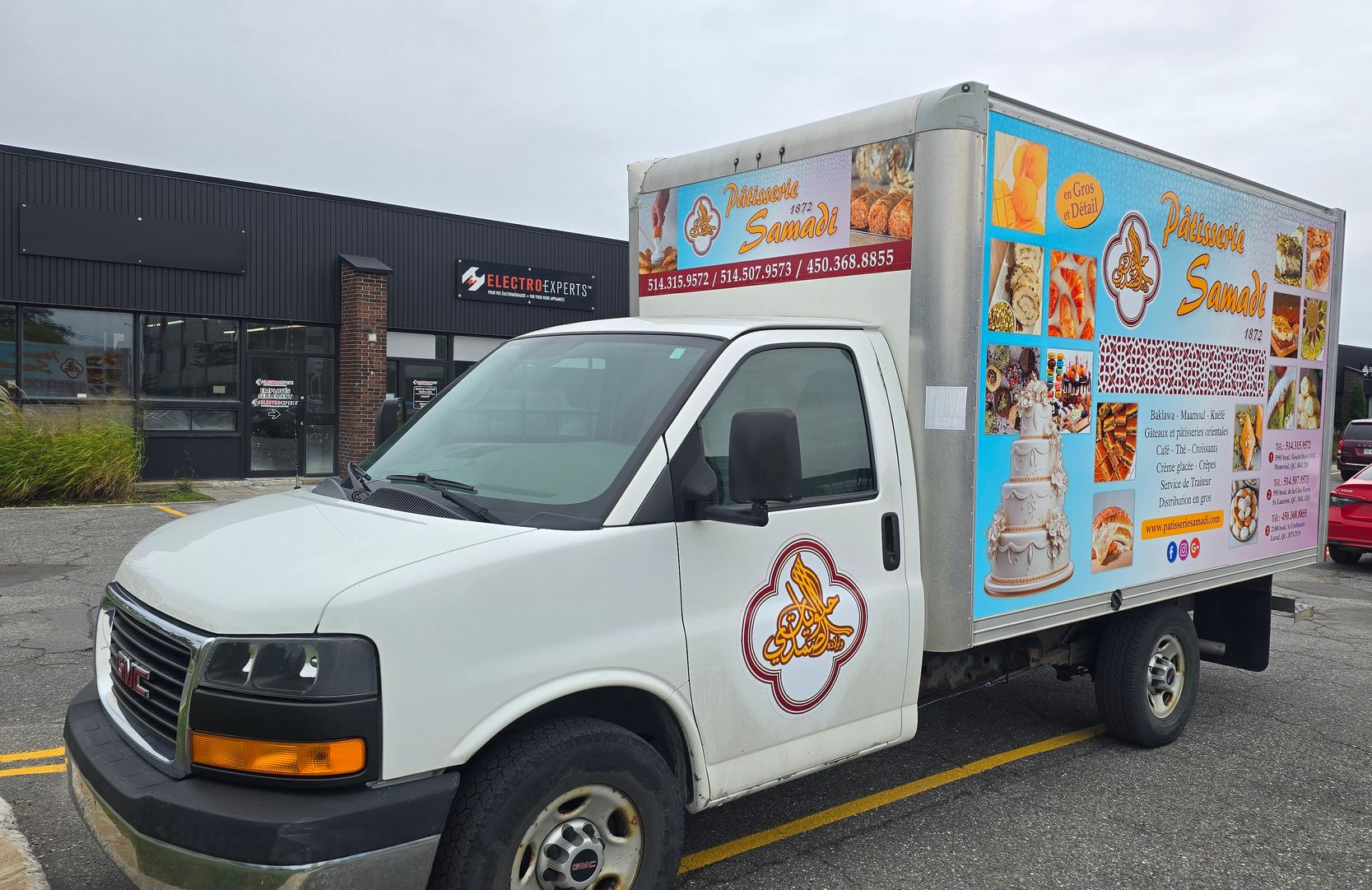 Food truck blanc avec publicité stationné devant un bâtiment.