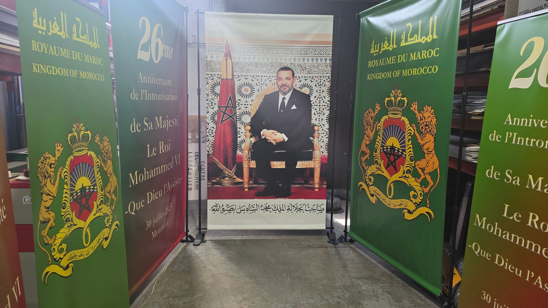 King Mohammed VI portrait flanked by green banners with Arabic text and a Moroccan emblem.