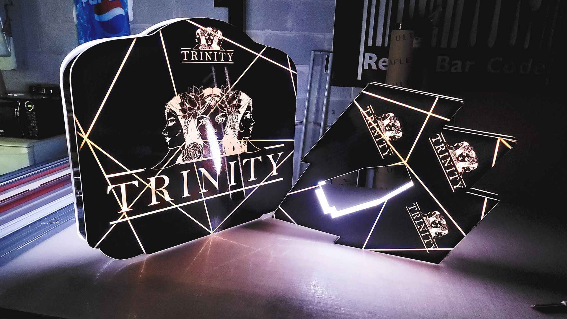 Panneaux avec logo Trinity noir et or sur une surface réfléchissante.