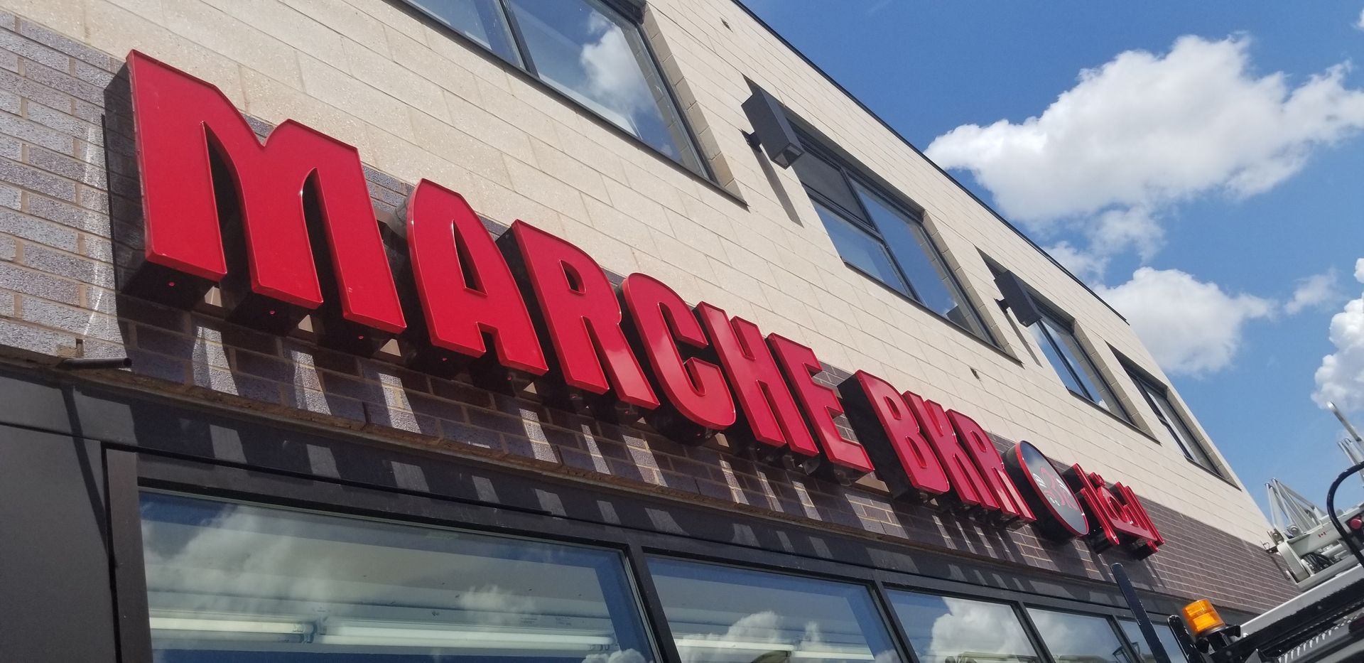 Enseigne au néon rouge du Marché Bon sur un bâtiment en briques sous un ciel bleu.