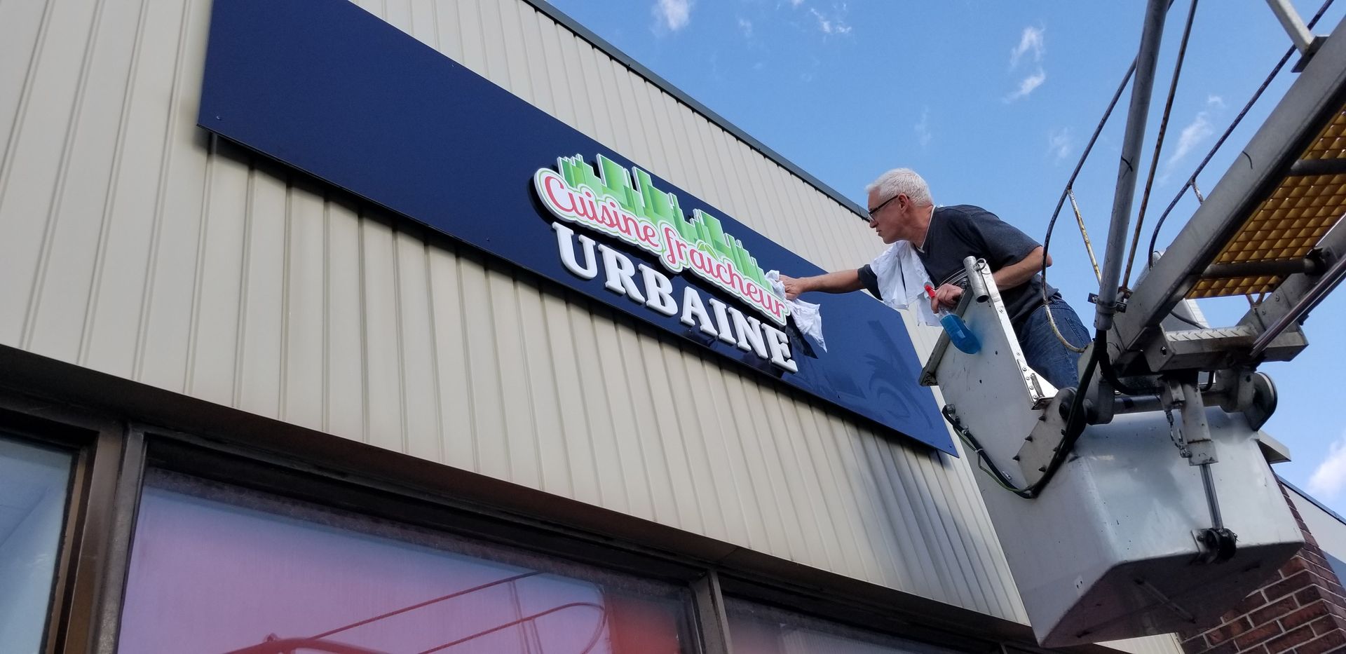 Un homme dans un ascenseur nettoie un panneau bleu sur lequel est écrit « URBAINE »