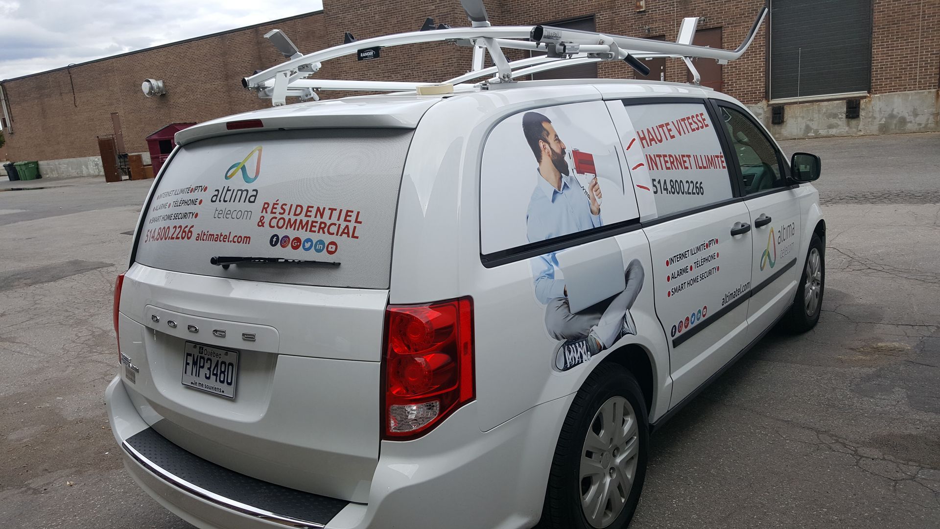 White service van with ladder rack, branded with company logo and contact info, parked outside a brick building.