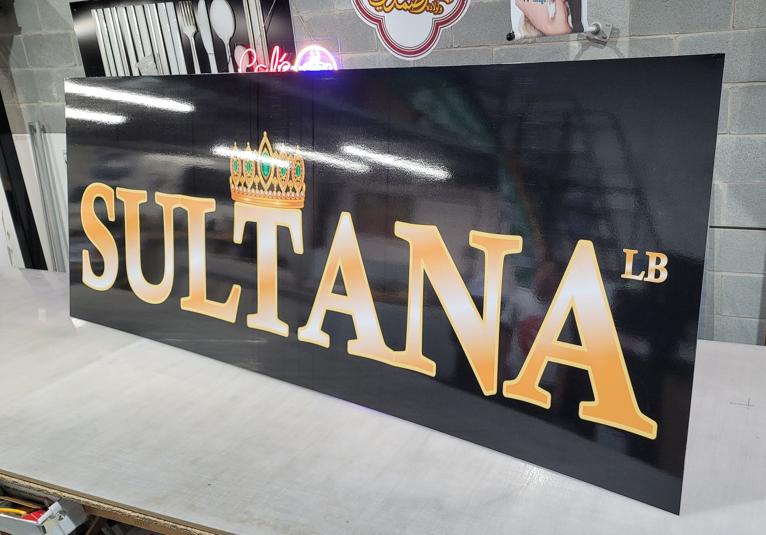 Grand panneau noir avec lettrage doré « SULTANA LB » et logo couronne doré.
