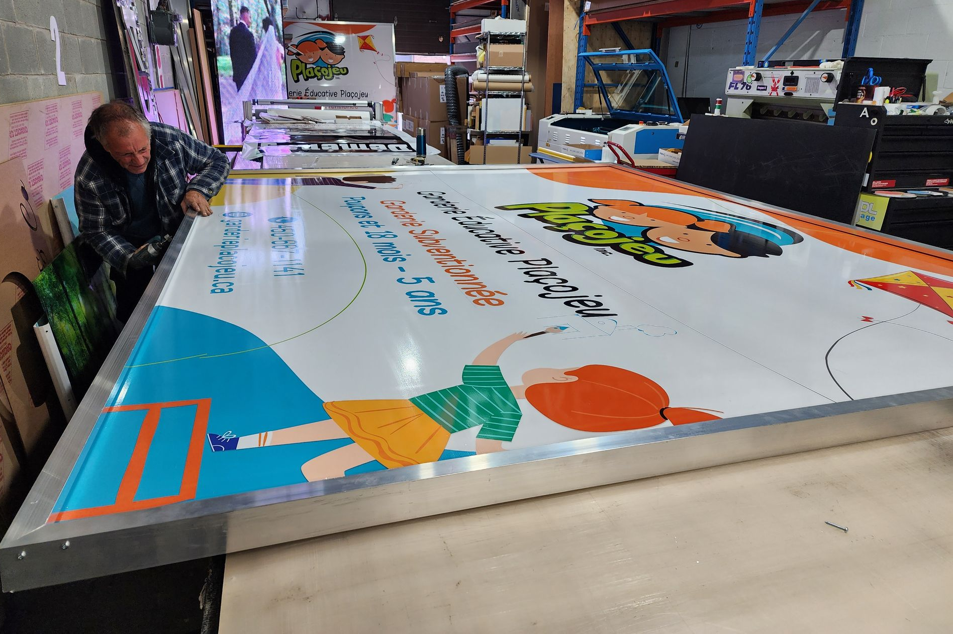 Un homme travaille sur un grand panneau coloré dans un atelier.