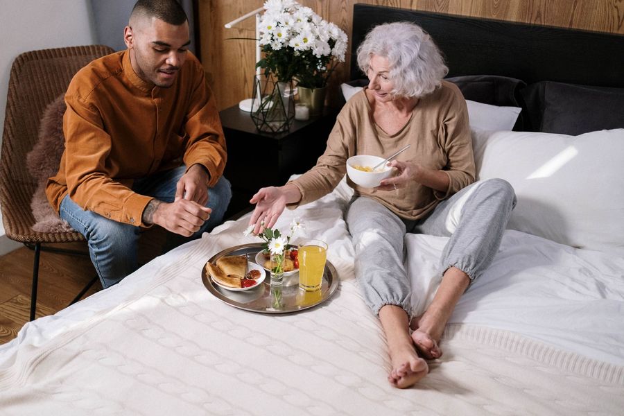 A man and a woman are sitting on a bed eating breakfast.