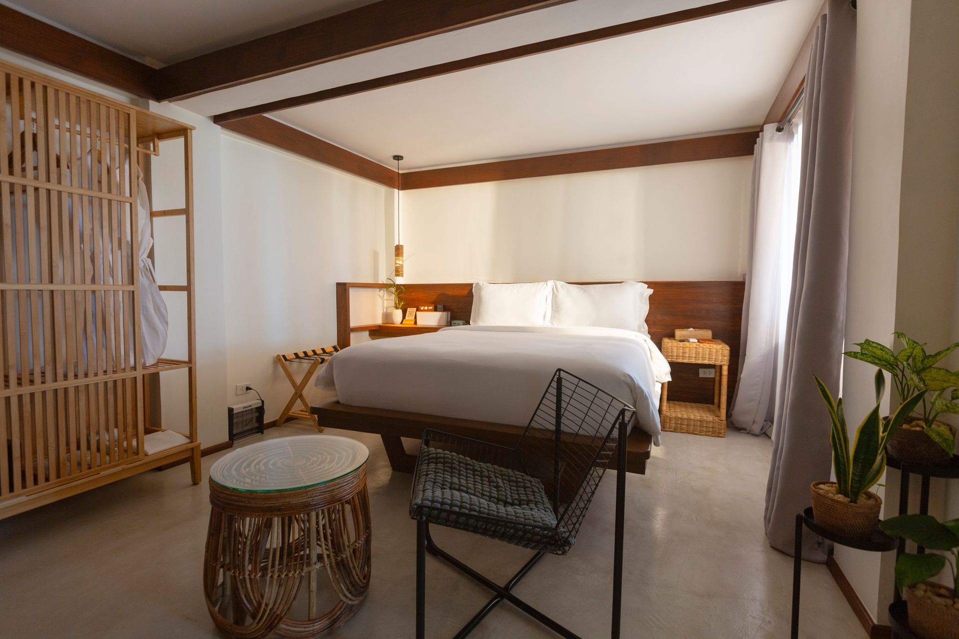 A hotel room with a bed , chair , table and plants.